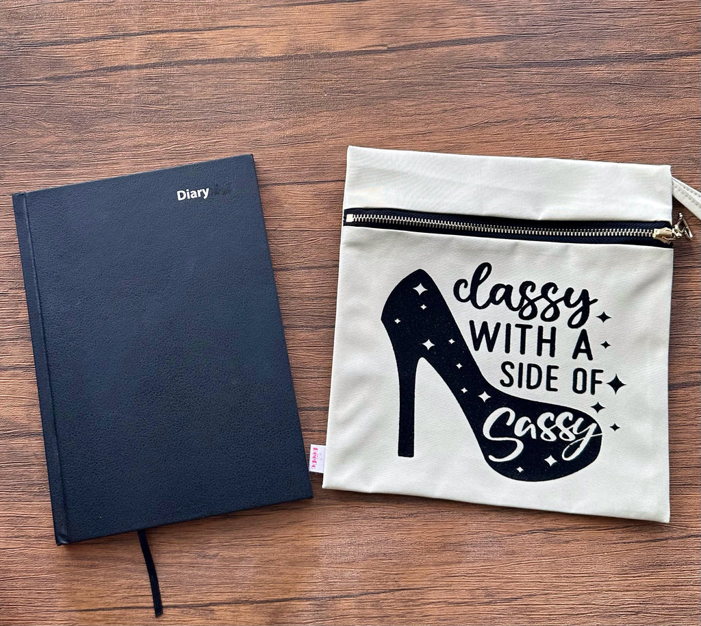 Black diary and white pouch with high heel design on a wooden surface