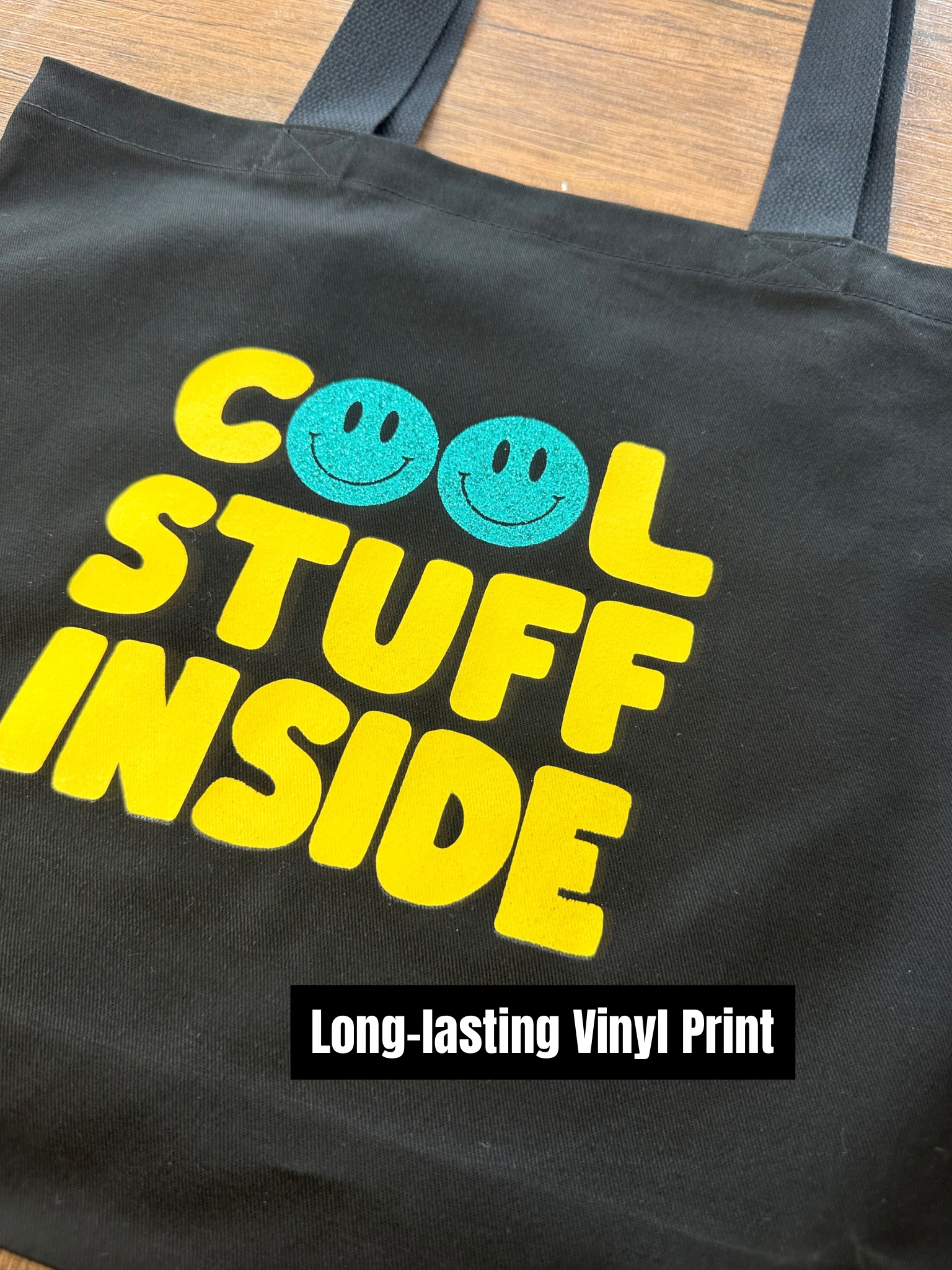 Black tote bag with 'Cool Stuff Inside' text and smiley faces on a wooden surface.