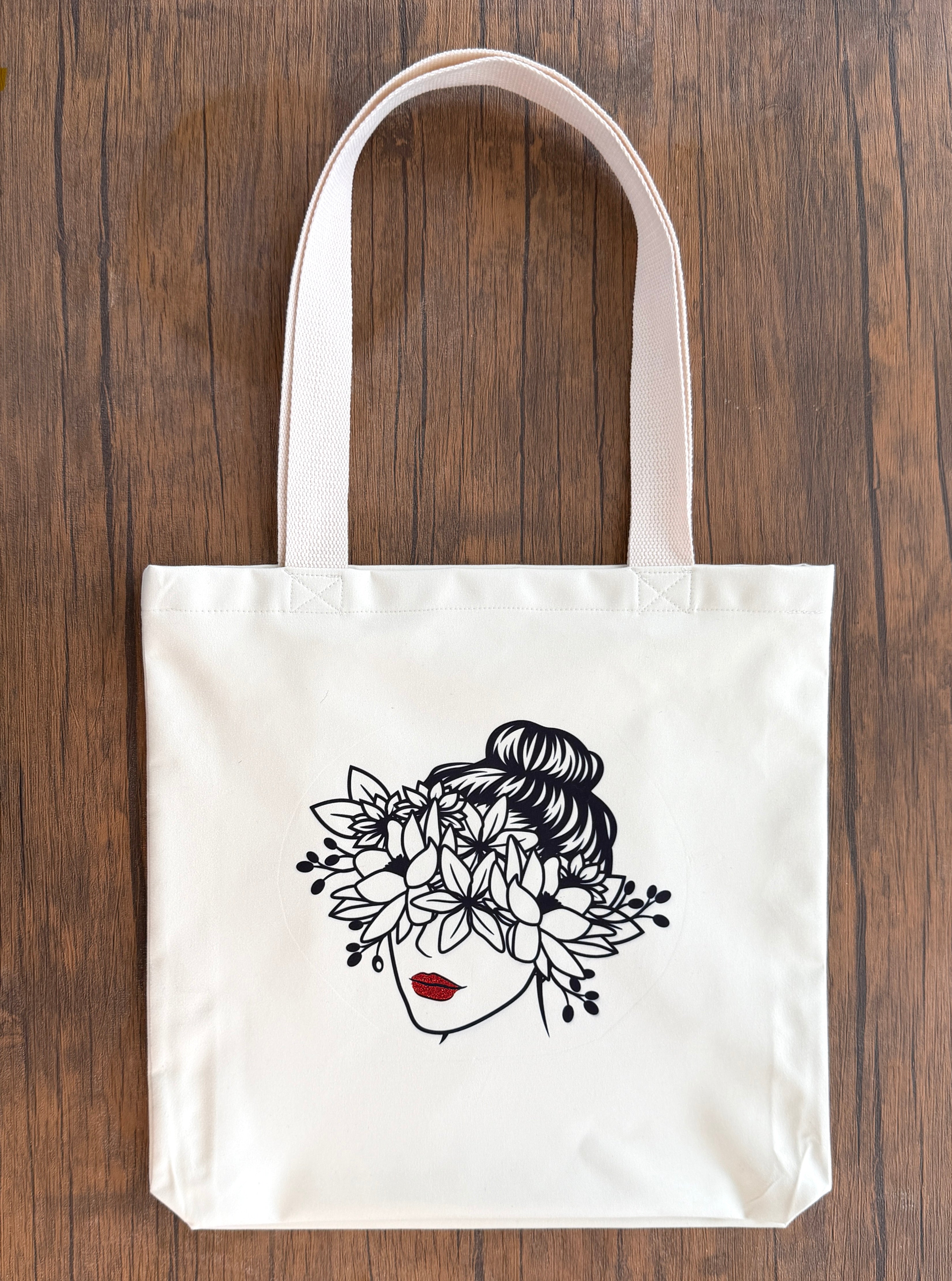 White tote bag with a black floral design on a wooden surface