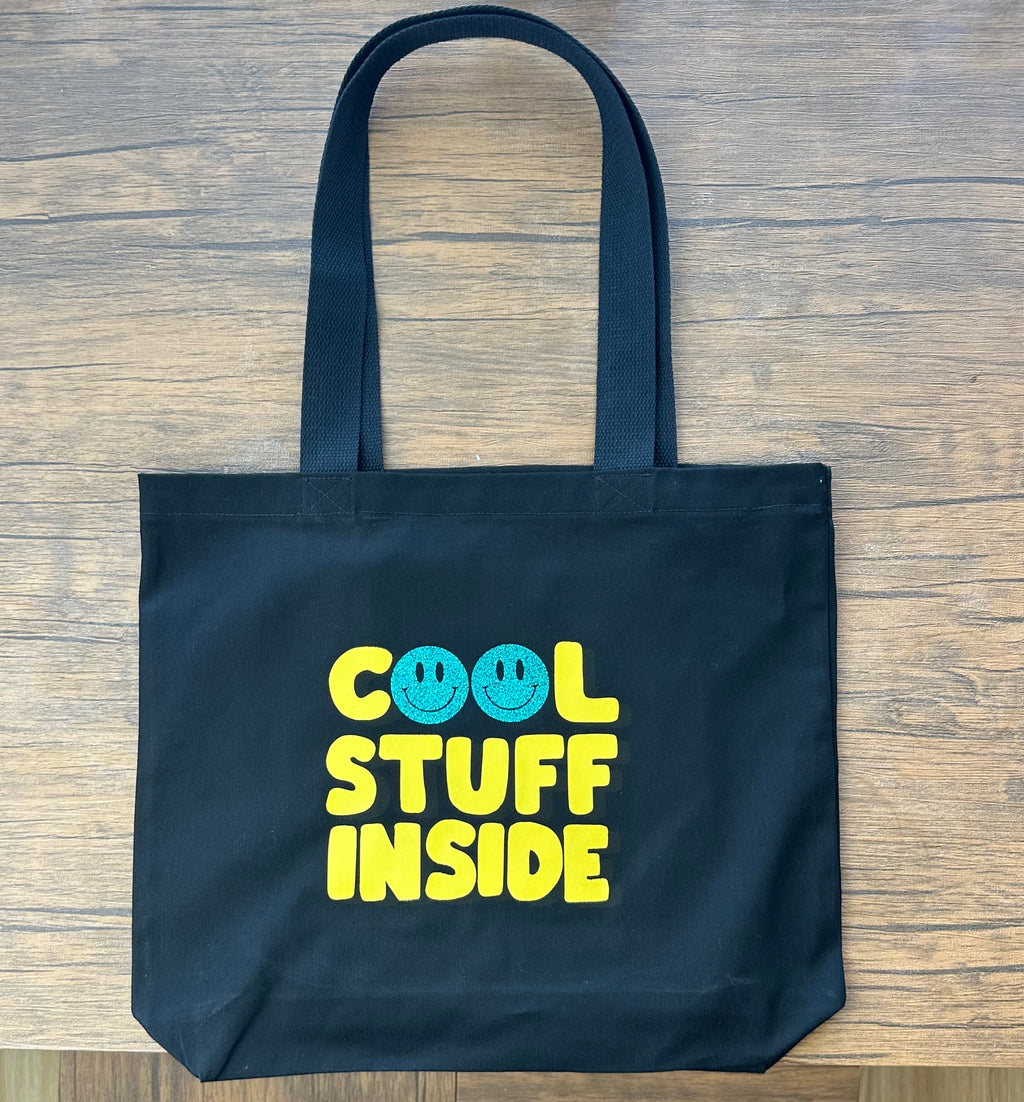 Black tote bag with 'Cool Stuff Inside' text on a wooden surface