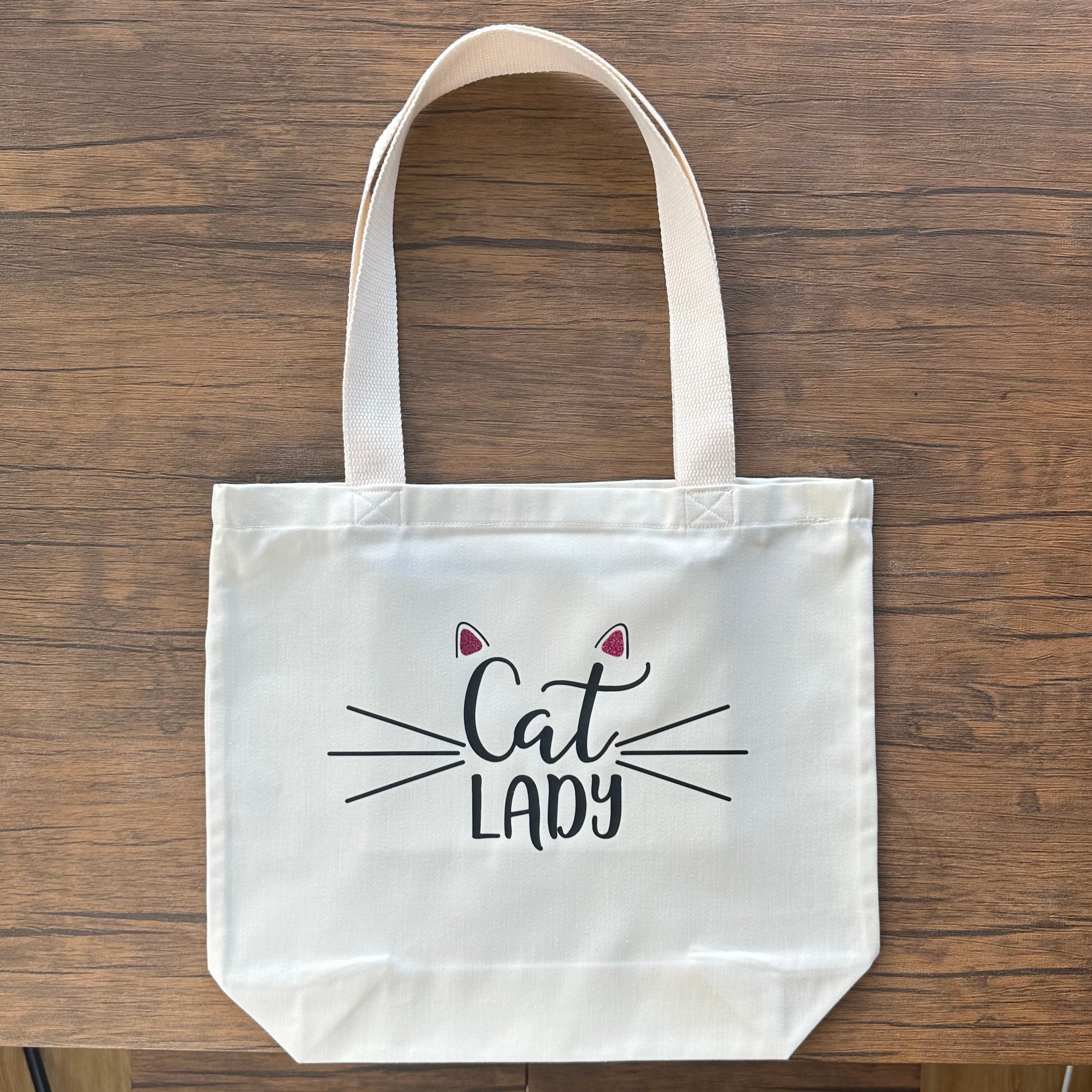 White tote bag with 'Cat Lady' text on a wooden surface, handmade cat lady tote bag made in the UK, gift for cat lovers