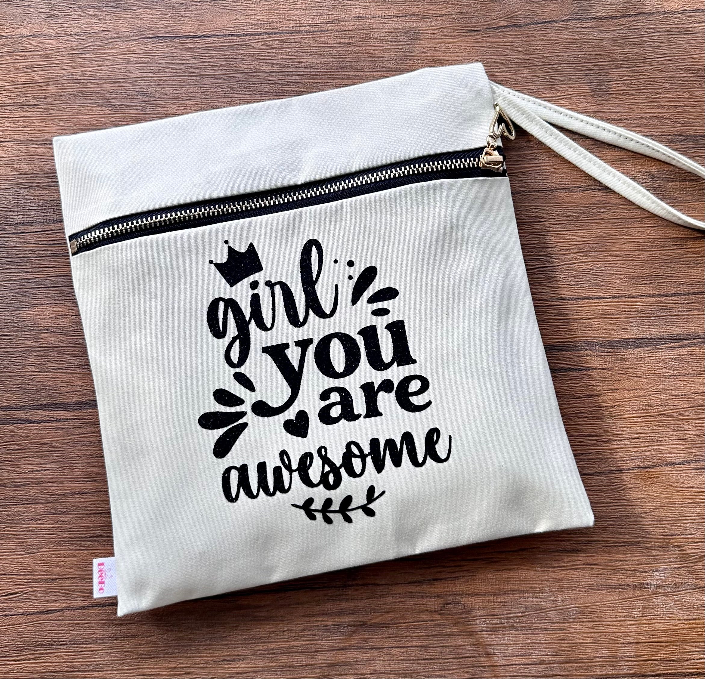 White pouch with 'girl you are awesome' text on a wooden surface