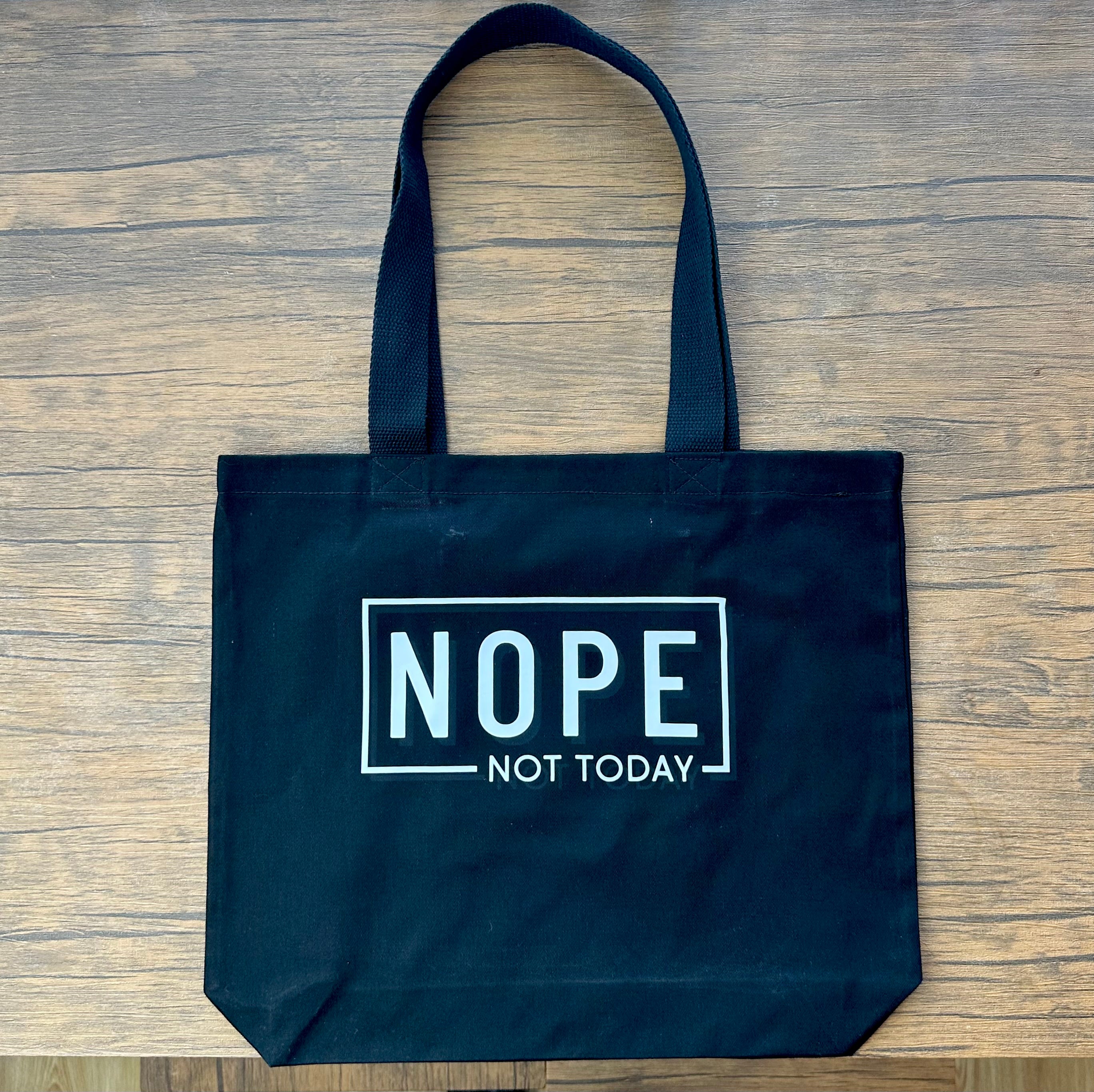 Black tote bag with 'NOPE NOT TODAY' text on a wooden surface