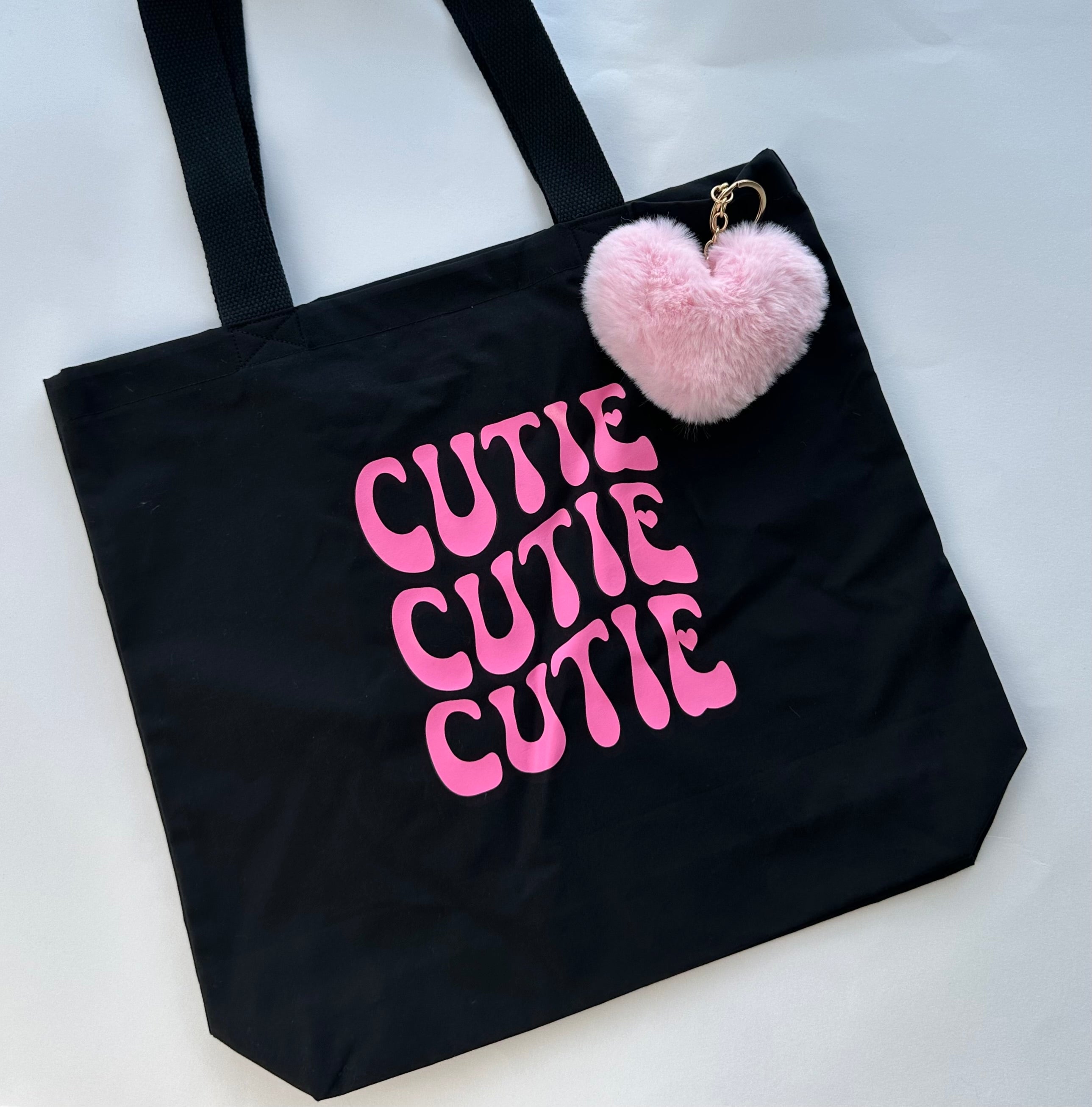 Black tote bag with pink 'CUTIE CUTIE CUTIE' text and a pink heart-shaped pom-pom on a white background, handmade gift for her UK