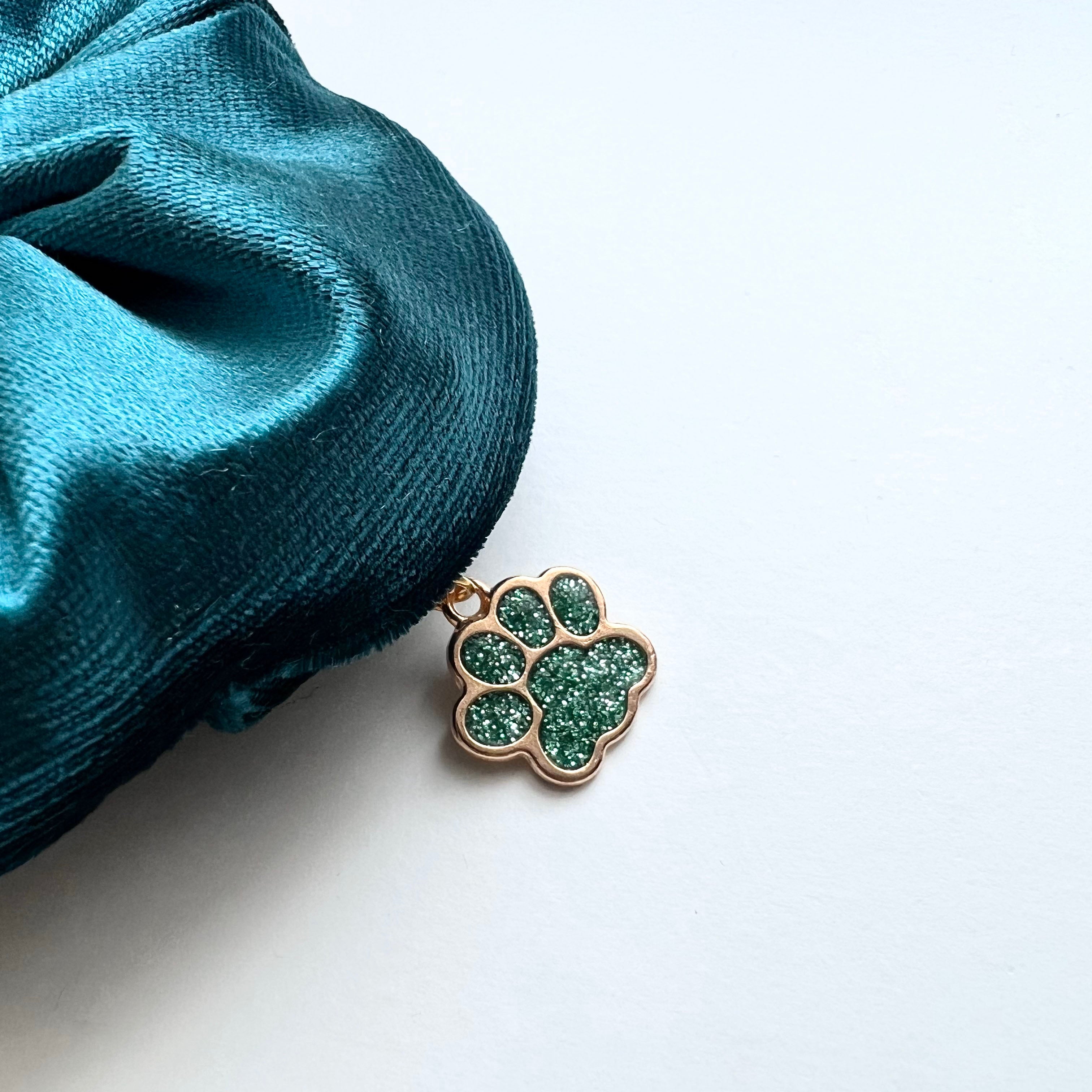 Gold paw-shaped pendant with green gemstones on a white background