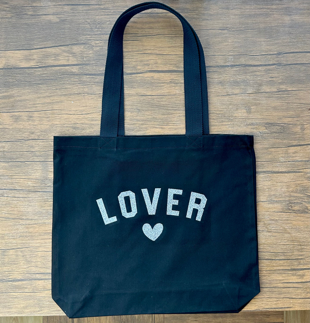 Black tote bag with 'LOVER' text and heart on a wooden surface