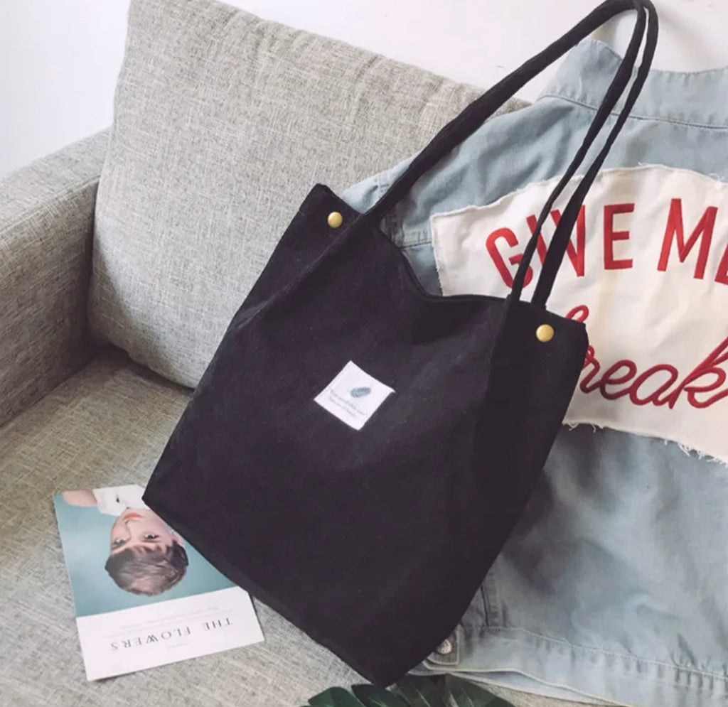 Black tote bag with a logo on a gray couch with a denim jacket and magazine.