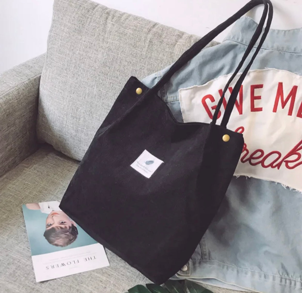 Black tote bag with a logo on a gray couch with a denim jacket and magazine.