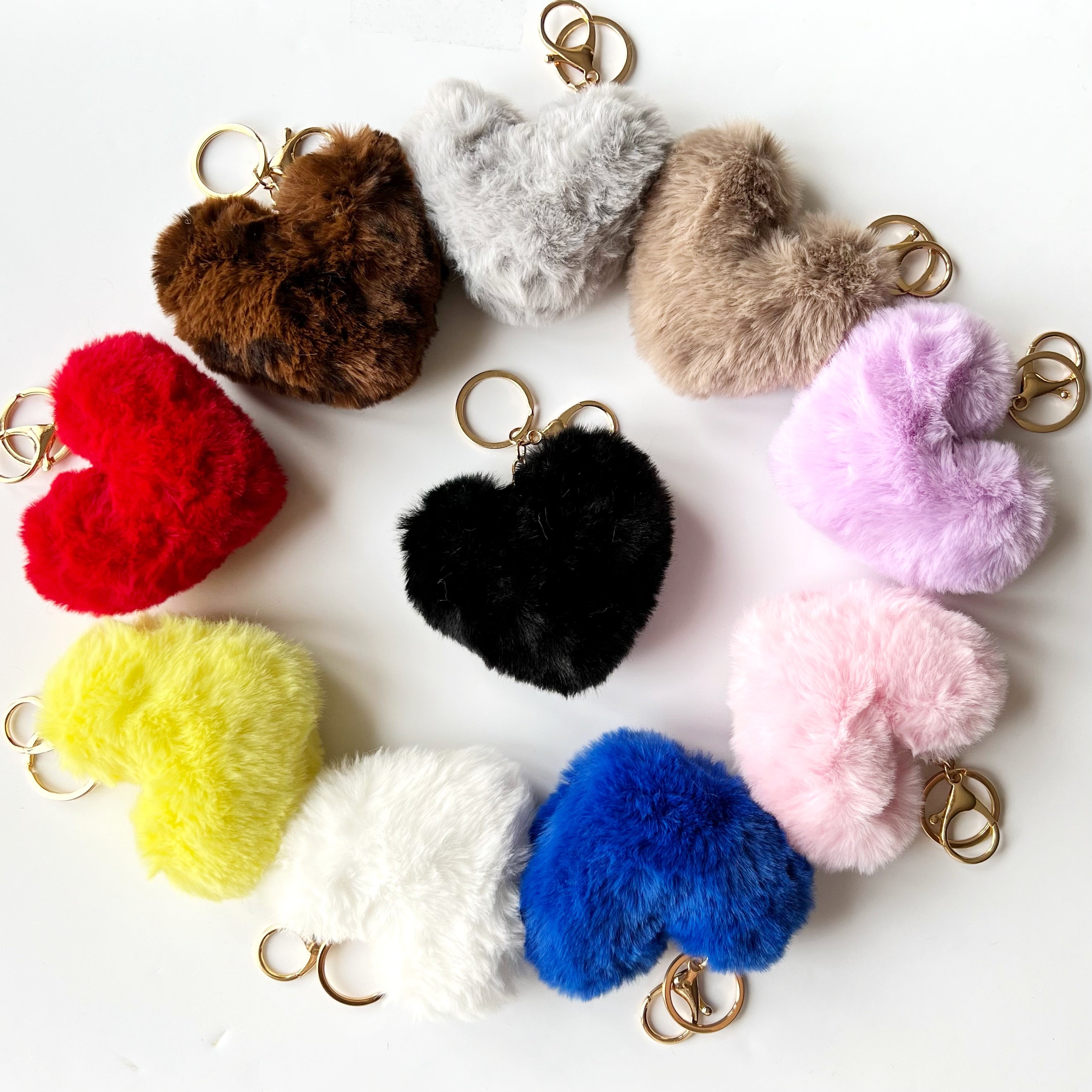 Colorful heart-shaped fuzzy keychains arranged in a circular pattern on a white background.