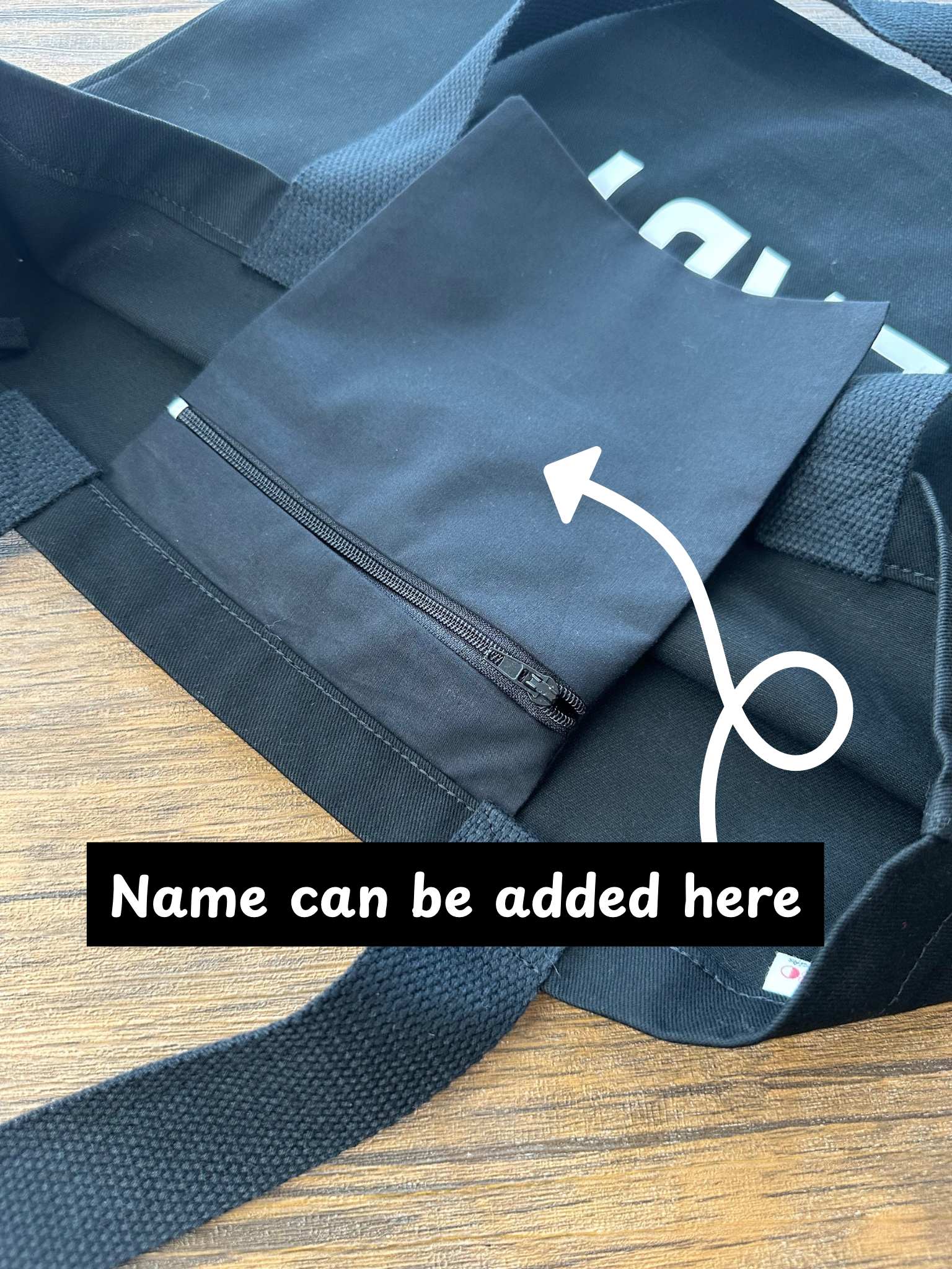 Black bag with a zipper on a wooden surface, with text indicating customization. Special gift for her UK