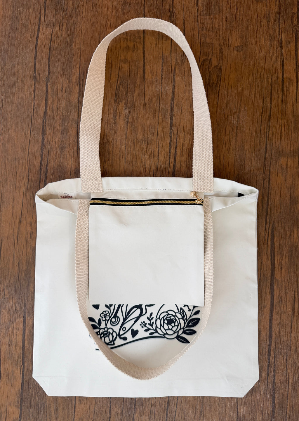 White tote bag with black floral design on a wooden surface