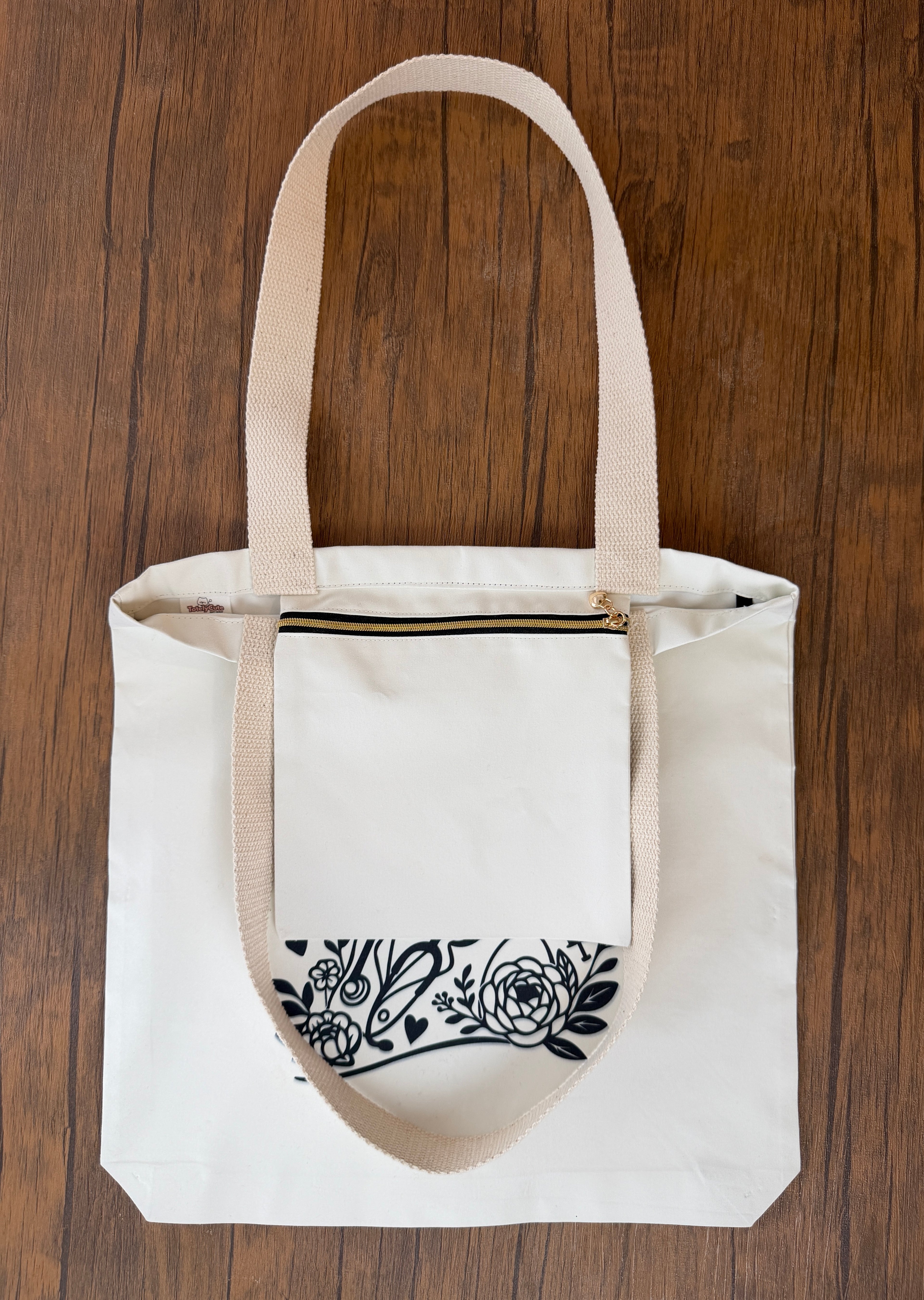 White tote bag with black floral design on a wooden surface