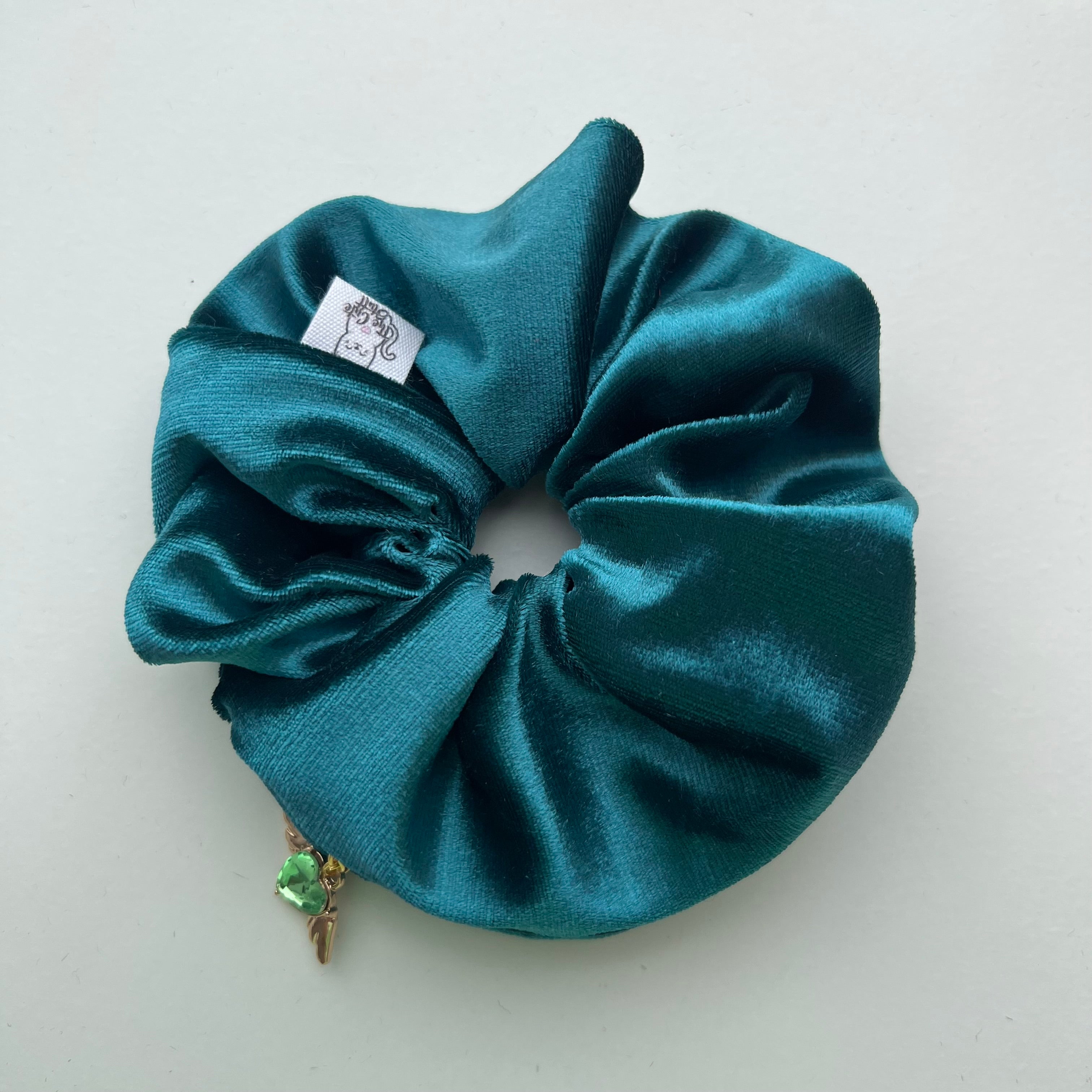 Teal scrunchie with a small decorative item on a light gray background. Scrunchie with zip pocket
