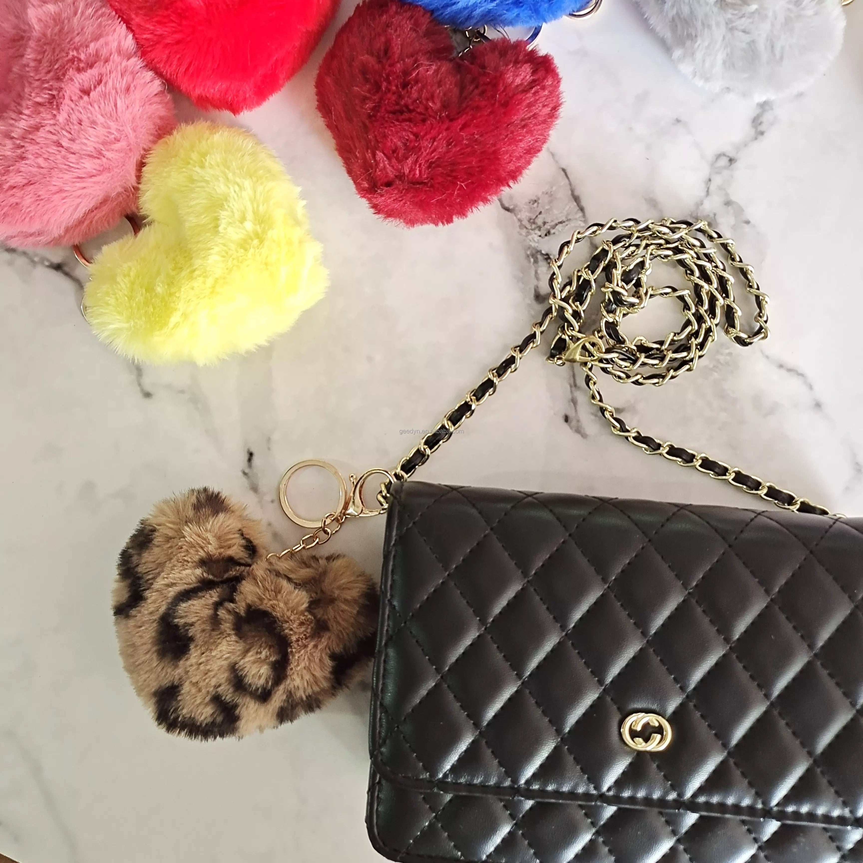 Black quilted handbag with gold chain strap and colorful pom-pom keychains on a marble surface